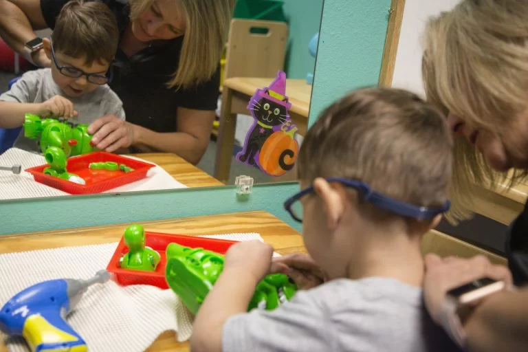 A woman is providing pediatric therapy to a child in a playroom. A woman is providing pediatric therapy to a child in a playroom.