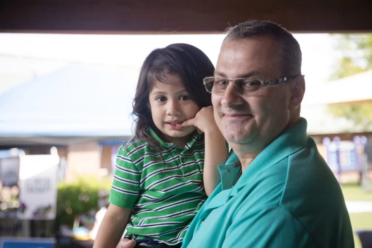 A man holding a young boy with cerebral palsy in a green shirt during pediatric therapy. A man holding a young boy with cerebral palsy in a green shirt during pediatric therapy.