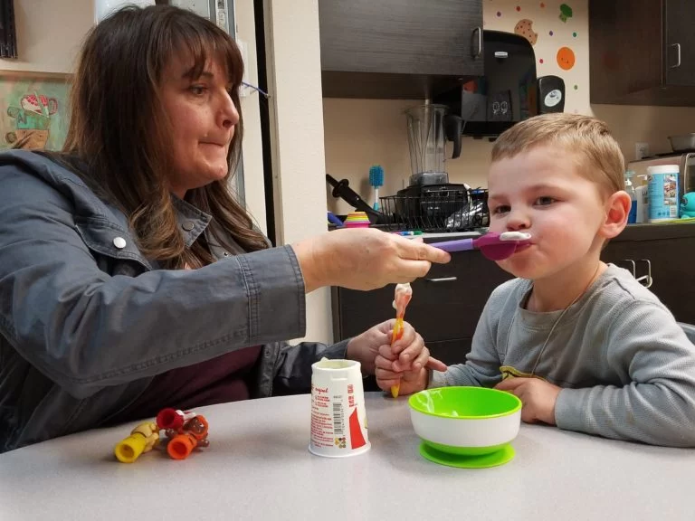 A woman is providing pediatric therapy by feeding a child with a spoon. A woman is providing pediatric therapy by feeding a child with a spoon.