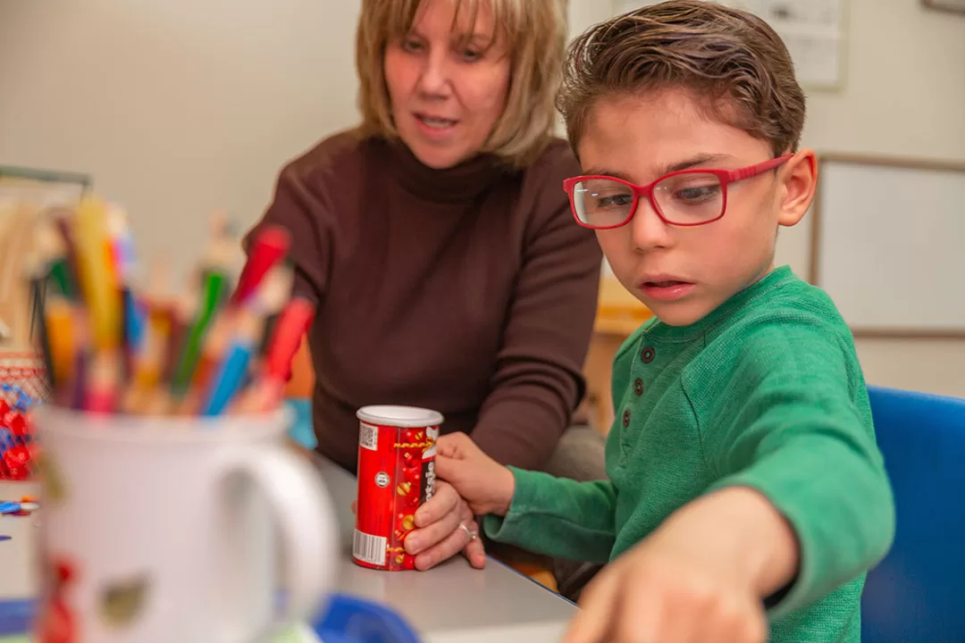 A young boy with cerebral palsy of Arizona is working with a teacher in a classroom. Sebastian with our Director of Therapy