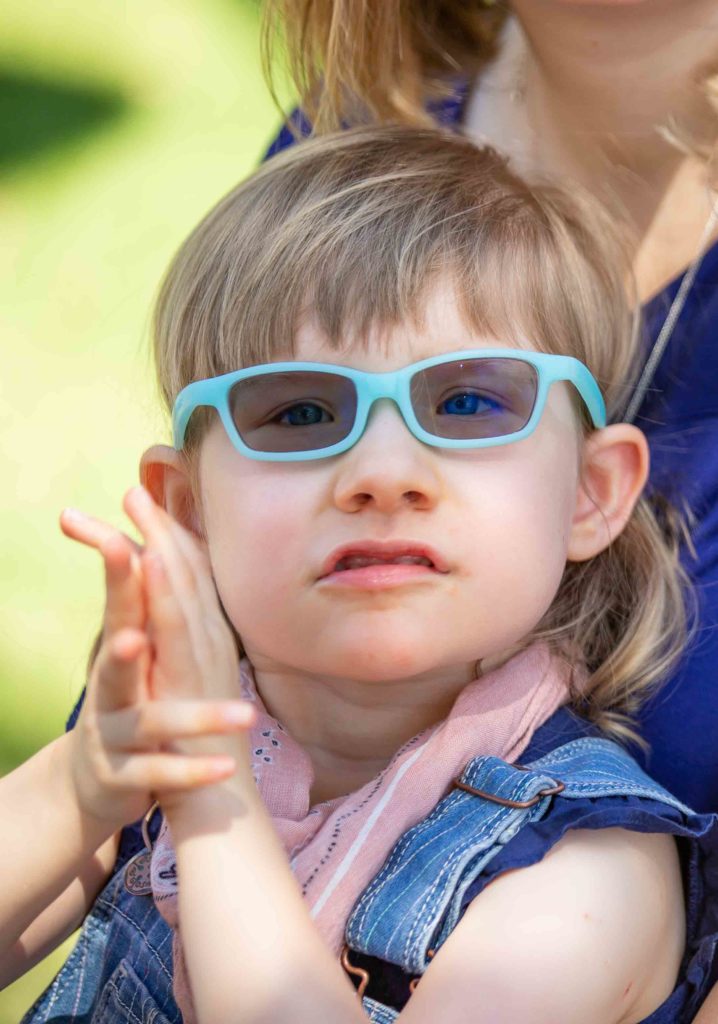 A young girl with cerebral palsy, wearing glasses, clapping her hands at a pediatric therapy session. A young girl with cerebral palsy, wearing glasses, clapping her hands at a pediatric therapy session.