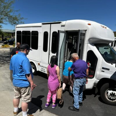 A group of people, participating in adult day programs, board a small white bus. Arizonability individuals going out on a local fishing trip at Cortez Park