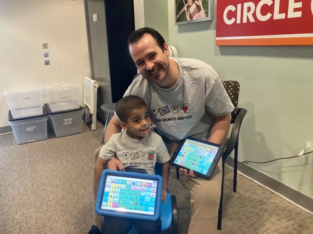 A man and a child sitting on a blue chair engaging in pediatric therapy with ipads. A man and a child sitting on a blue chair engaging in pediatric therapy with ipads.