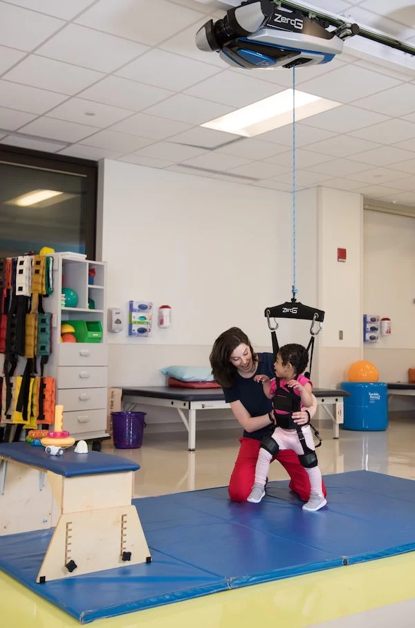 A woman is providing pediatric therapy to a child on a swing in an early learning center. A woman is providing pediatric therapy to a child on a swing in an early learning center.