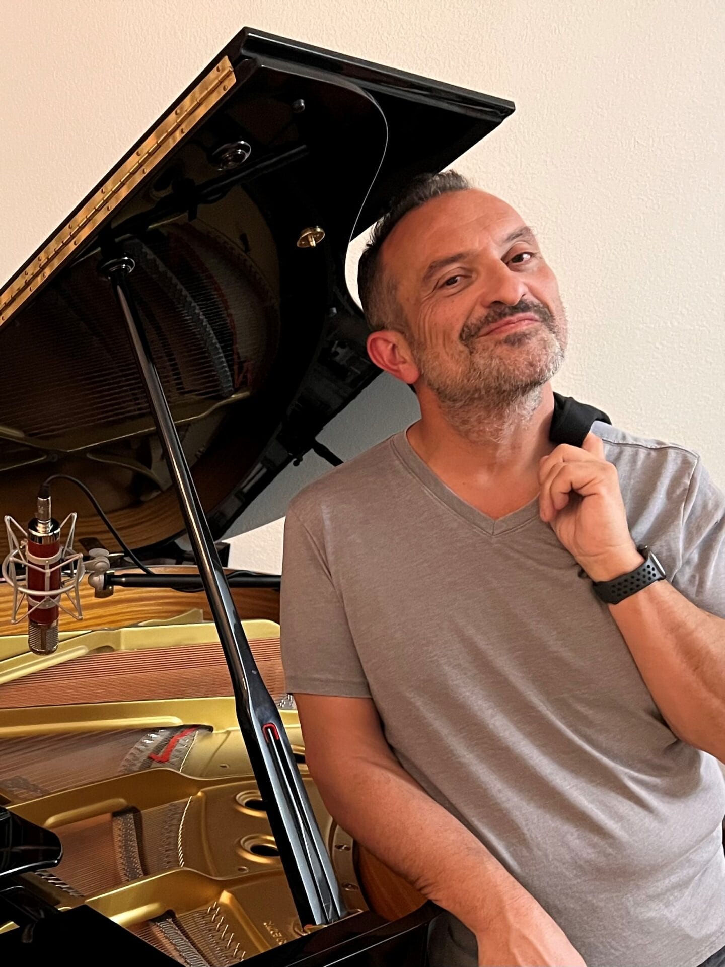 Carl Herrgesell Carl Herrgesell smiling, leaning on a grand piano with its lid open, touching his chin thoughtfully, in a room with a beige wall, representing the united cerebral palsy of central Arizona.