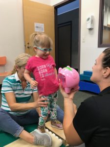 A little girl is engaged in pediatric therapy while playing with a piggy bank. A little girl is engaged in pediatric therapy while playing with a piggy bank.
