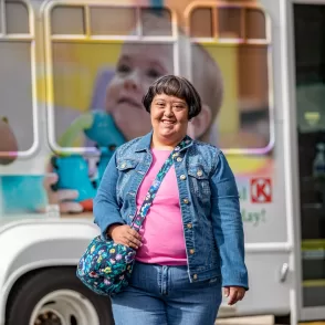 A woman with cerebral palsy standing in front of a bus, potentially accessing home and community based services or pediatric therapy.