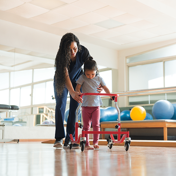 A woman is assisting a child with a walker at a gym, providing home and community based services through the Cerebral Palsy of Arizona.