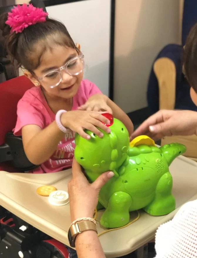 A young girl with cerebral palsy is playing with a toy dinosaur during a pediatric therapy session at home. A young girl with cerebral palsy is playing with a toy dinosaur during a pediatric therapy session at home.