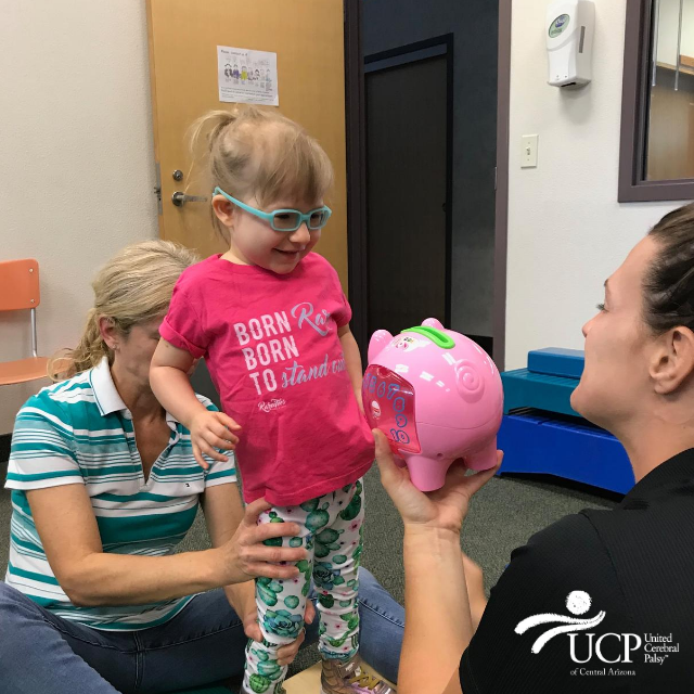 A young girl with cerebral palsy of Arizona is playing with a pink piggy bank at an early learning center.